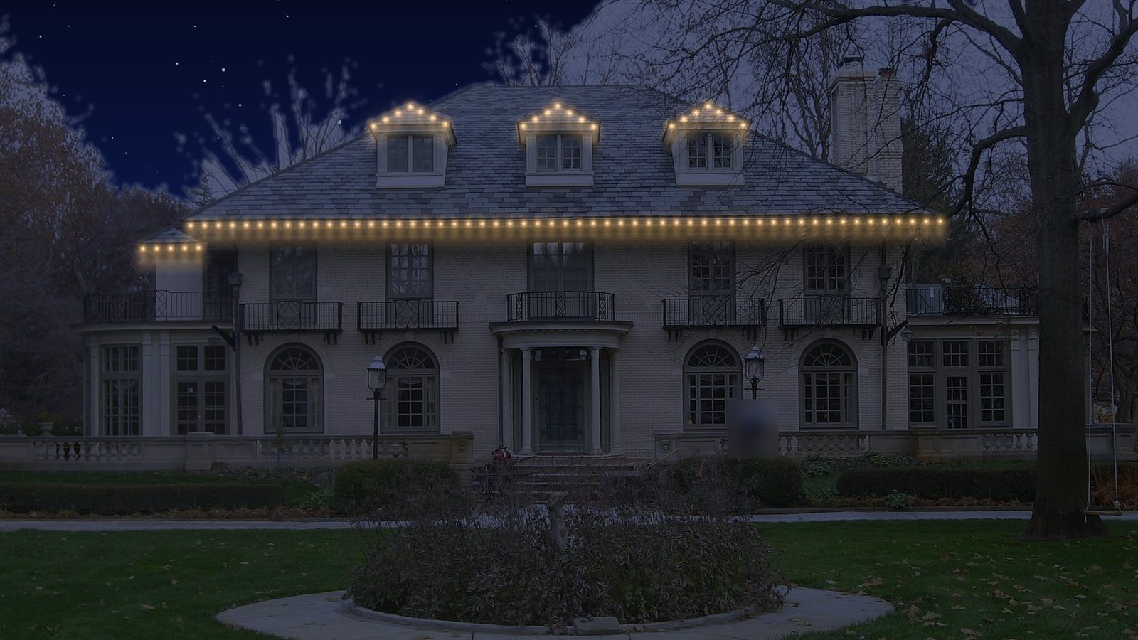 A stone home with warm white permanent lights under the roof edge and dormers.
